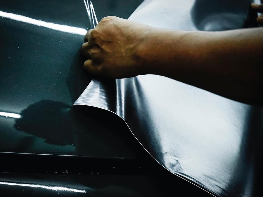 A close-up of dark film being worked over a curved panel with a heat gun in frame.
