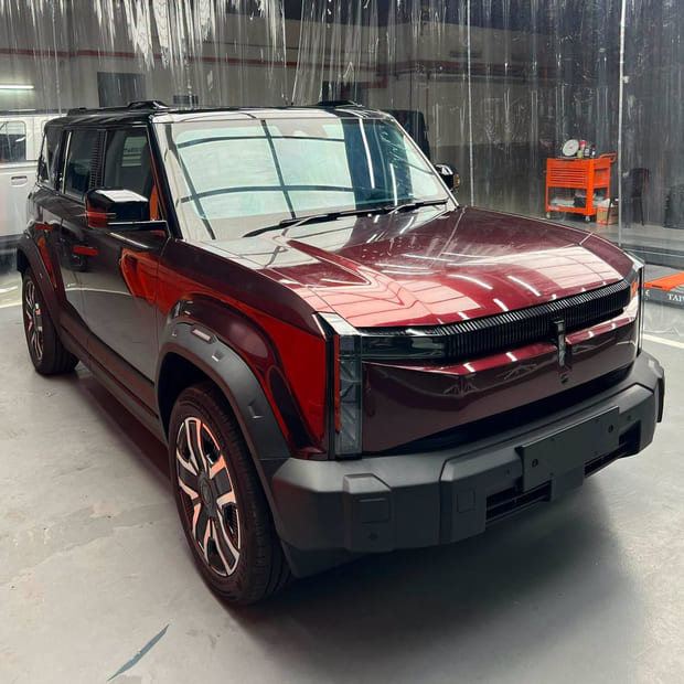 An iCaur 03 electric SUV in the workshop in front of hanging clear PVC strip curtains, finished in a deep liquid red.