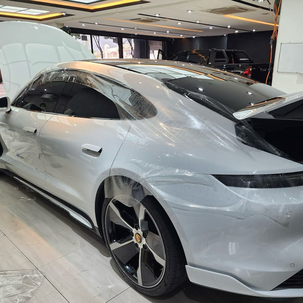 A Porsche Taycan from a high side three-quarter in a wood-lined bay, in silver.